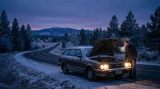 A car stranded on the side of a snowy road in winter, illustrating the problem of a dead car battery in freezing weather.