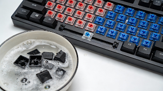 Mechanical keyboard switches exposed during cleaning process with keycaps soaking in a bowl.