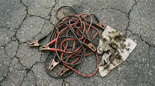 A tangled mess of traditional jumper cables, representing the inconvenience of the old method for jump-starting a car.