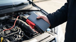 A person holding a modern portable car jump starter, demonstrating its compact size and ease of use.