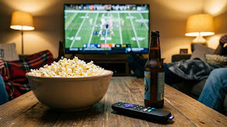Roku Streaming Stick 4K remote on a coffee table with popcorn and football game on TV background for Super Bowl party hosting.