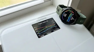 Garmin Index S2 smart scale with color display showing weight trend graphs, paired with a Garmin GPS running watch for ecosystem integration.