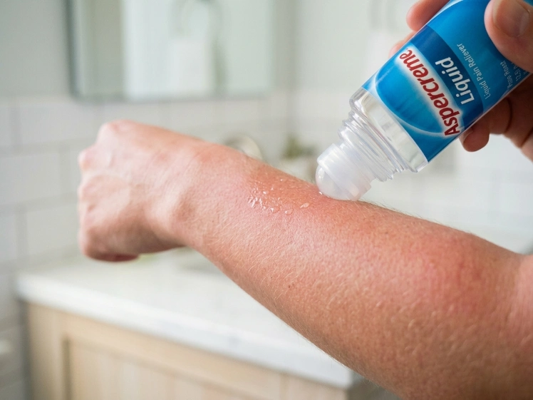 A close-up of a person using the Aspercreme Lidocaine roll-on applicator on a sunburned arm for mess-free relief.
