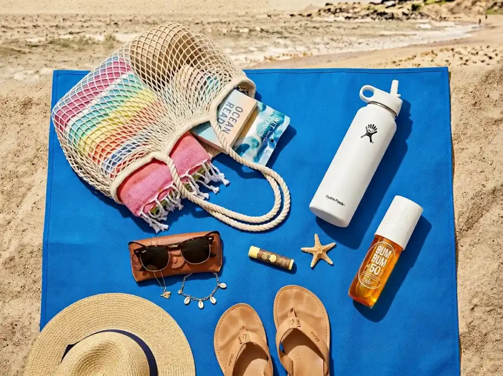 A collection of summer beach essentials organized on a sand-free mat, emphasizing a clean and organized beach setup.