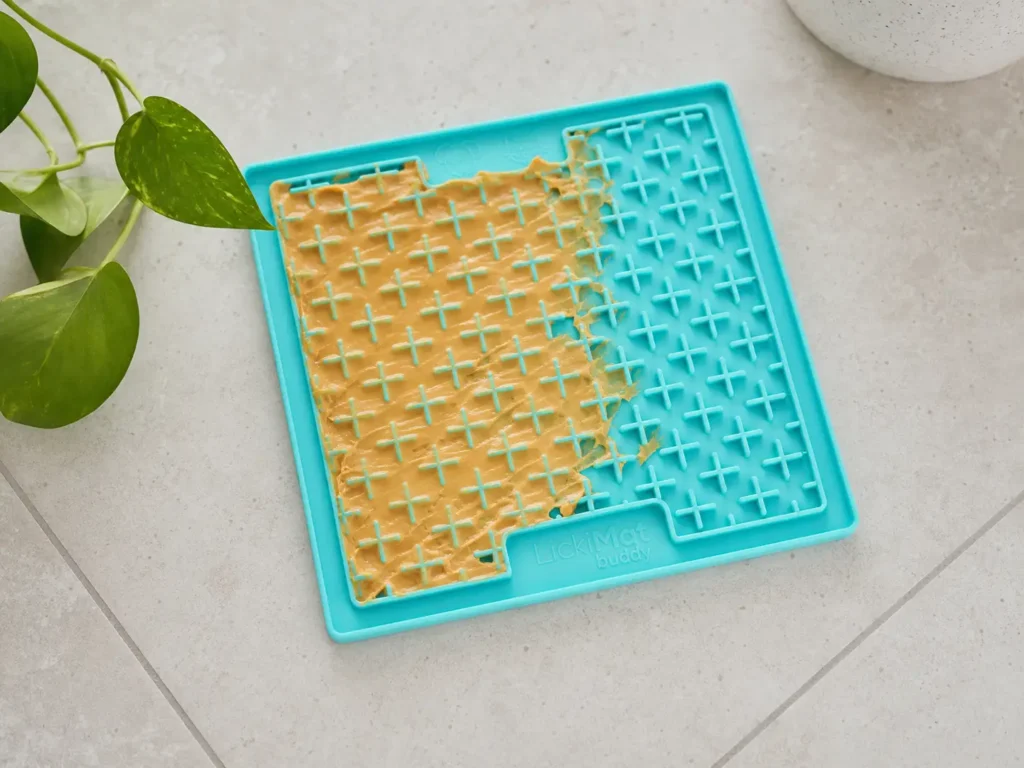 Turquoise LickiMat Classic Buddy dog lick mat with peanut butter spread on the textured surface.
