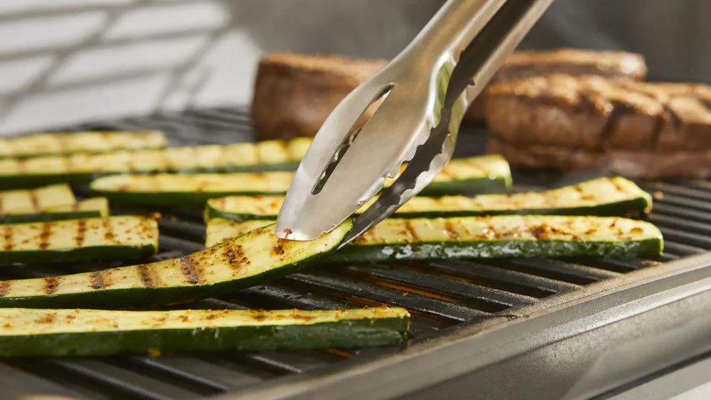 Weber 6630 Precision tongs carefully gripping an asparagus spear on a hot grill.