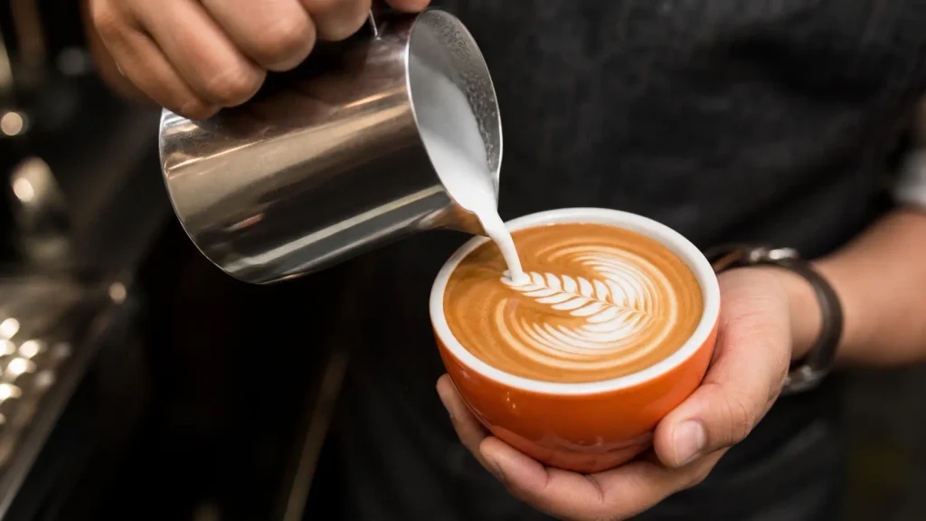 Pouring barista-quality microfoam from a pitcher into a pumpkin spice latte to create latte art.