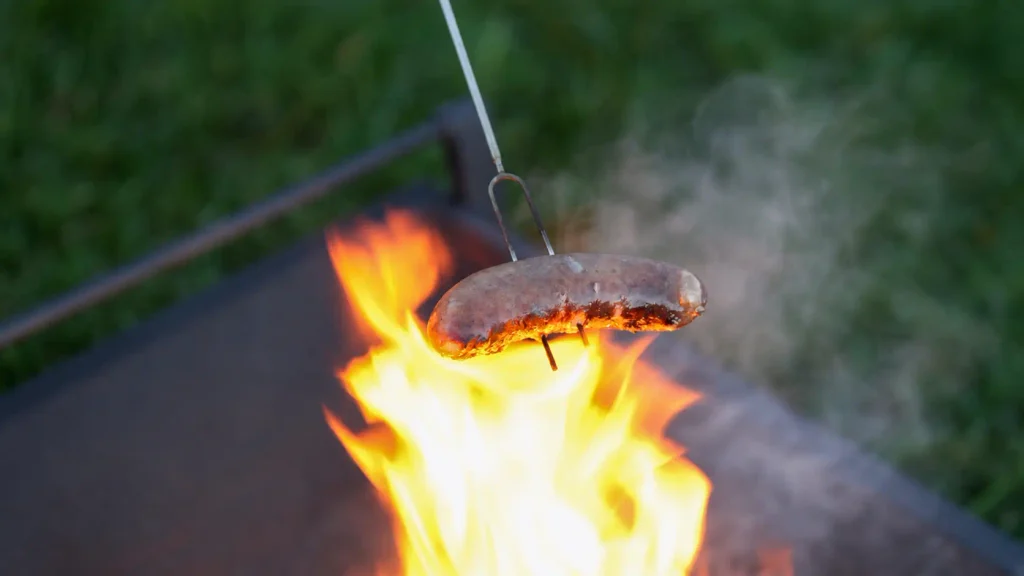 Tapirus heavy duty telescoping skewers roasting a thick sausage over glowing coals.